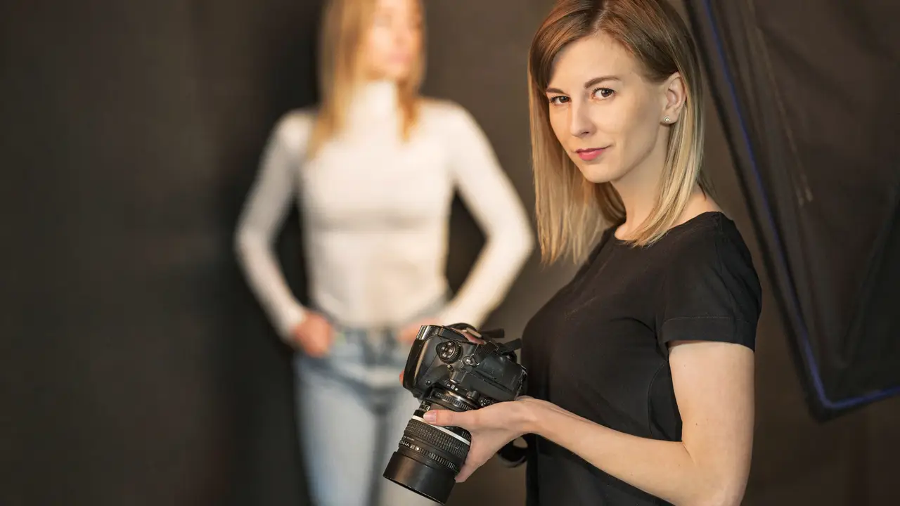 Fotografin mit Spiegelreflex-Kamera im Fotostudio. Im Hintergrund ein weibliches Model.