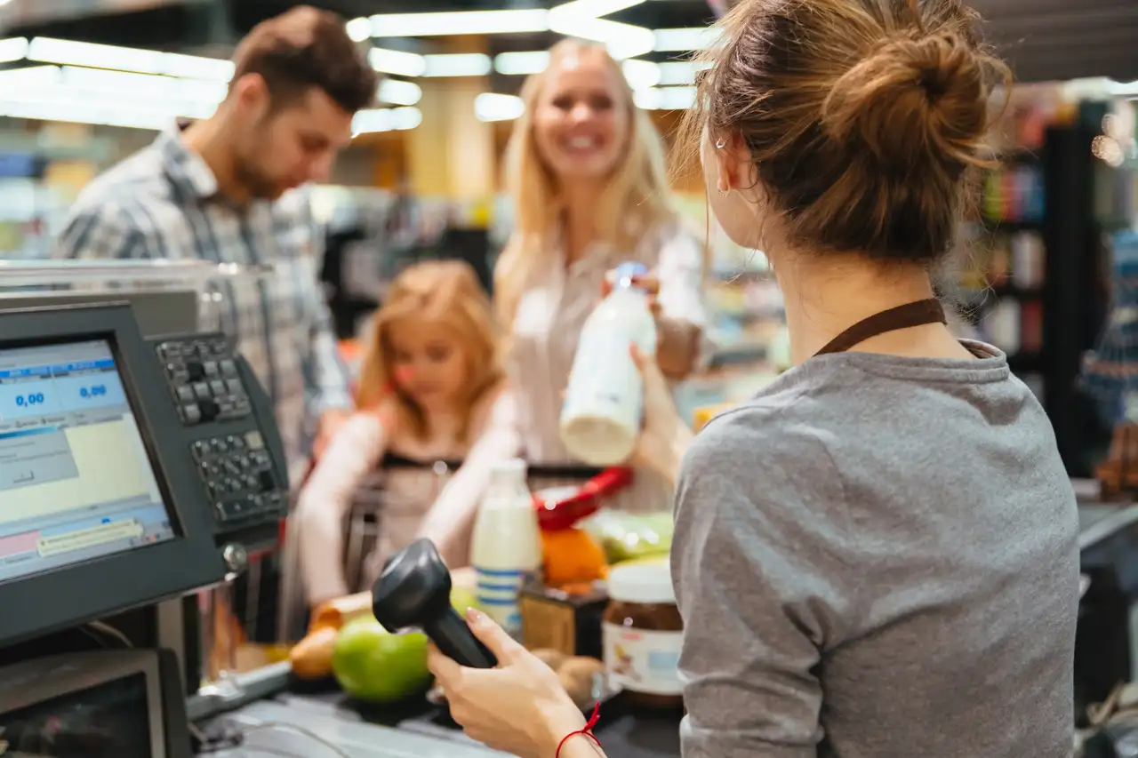 Supermarktkasse mit Kassiererin und einkaufenden Kunden zum Thema: Die größten Supermarktketten Deutschlands.